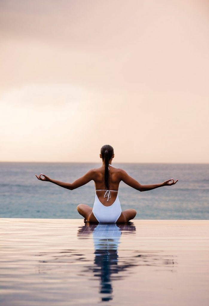 A woman sitting in front of the sea and sunset sitting down in the water doing a yoga pose