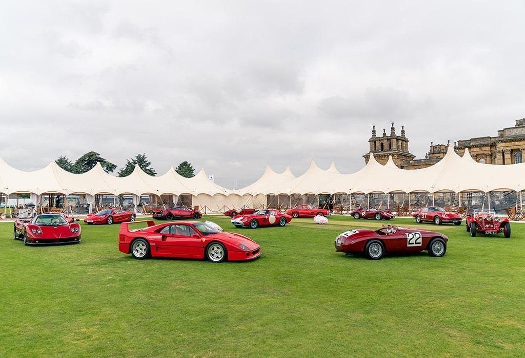 Many white marquees in the background behind many luxury red cars positioned in a circle